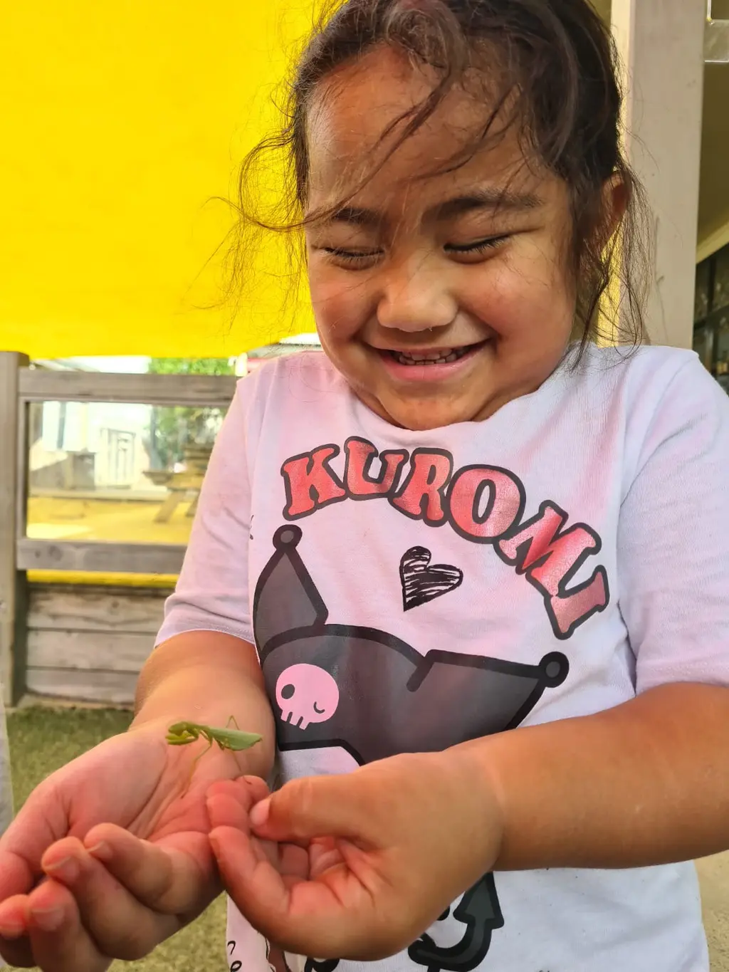 A smiling child holding a praying mantis gently in her hands at Paramount Grove.