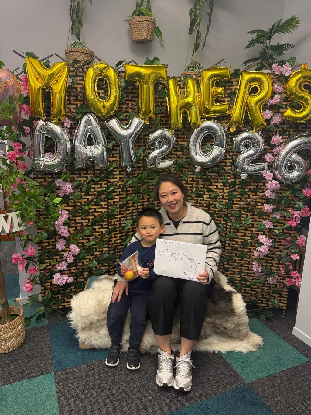 A child and caregiver smiling together in front of Paramount Grove's Mother's Day display.