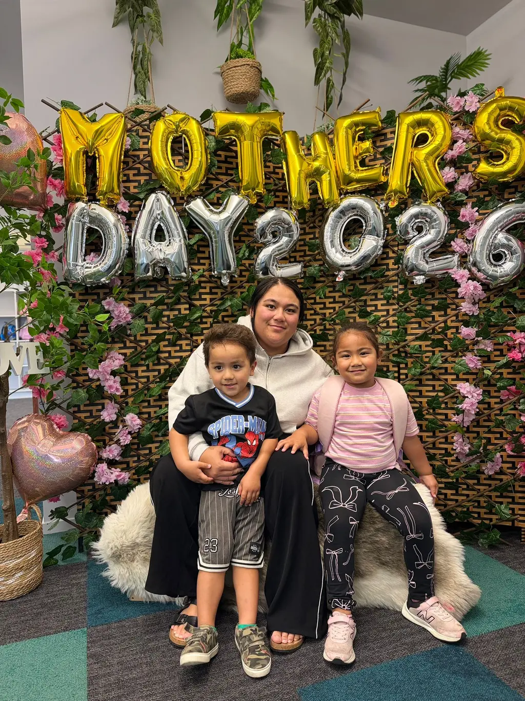 A caregiver and two children sitting together in front of the Mother's Day display at Paramount Grove.